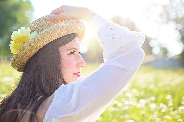 woman wearing a hat and walking through a meadow filled with daisies